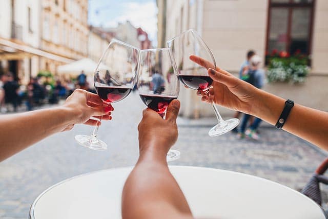 Wijn kado's 2 Drie handen klinken met glazen rode wijn buiten op straat met historische gebouwen.