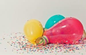 Voor wie kan jij wel een cadeau idee gebruiken? 6 Drie ballonnen in geel, blauw en roze liggen op een witte ondergrond met kleurrijk confetti.