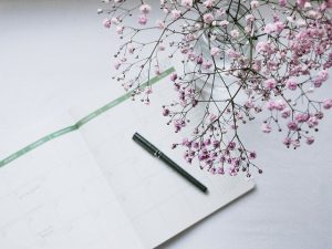 Webshop; Invulboekjes.nl 7 Opengeklapte maandkalender met pen en vaas met roze takken bloemen op witte achtergrond.