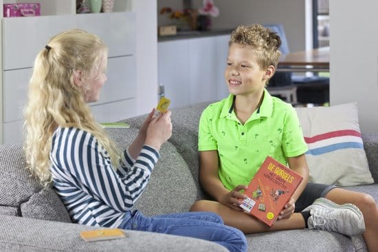 Twee kinderen zitten op een bank, meisje met kaart, jongen met boek, ze lachen naar elkaar.