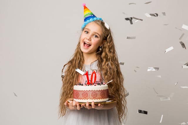 Meisje met kleurrijke feesthoed houdt verjaardagstaart met kaars cijfer 10 en vallende confetti.