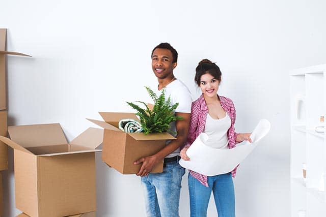 Man en vrouw met verhuisdozen en een groot vel papier in een lege kamer.
