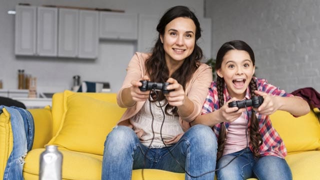 Dit zijn de leukste kindervriendelijke games! 11 Twee vrouwen op gele bank spelen samen videogames met gamecontrollers in handen.