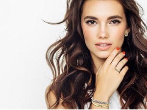 Sieraden als sinterklaascadeau 6 Jonge vrouw met lang golvend bruin haar, armband, ring en roodgelakte nagels tegen witte achtergrond.