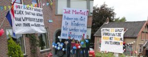 De leukste teksten voor een bruiloft spandoek! 3 Huisgevels met spandoeken over gezinskwesties en een groep mensen met ballonnen ervoor.