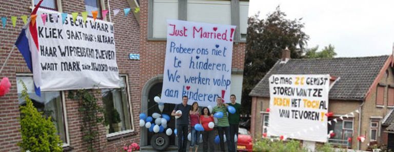 De leukste teksten voor een bruiloft spandoek! 2 Huisgevels met spandoeken over gezinskwesties en een groep mensen met ballonnen ervoor.