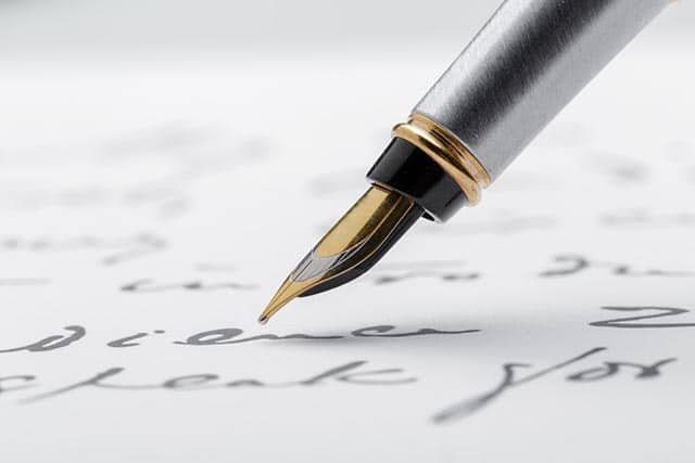 Close-up van een vulpen punt die handgeschreven tekst op papier nadert.