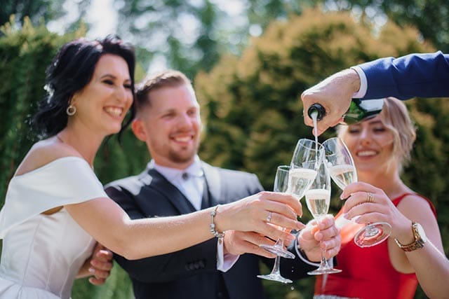 Feestreglement voor de bruiloft 3 Drie personen proosten met champagneglazen terwijl een vierde persoon inschenkt buitenshuis.