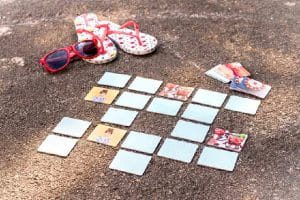 Dit zijn de leukste spellen met eigen foto's! 5 Rode slippers, rode zonnebril en een kaartspel met kaarten op een ruwe buitenvloer.