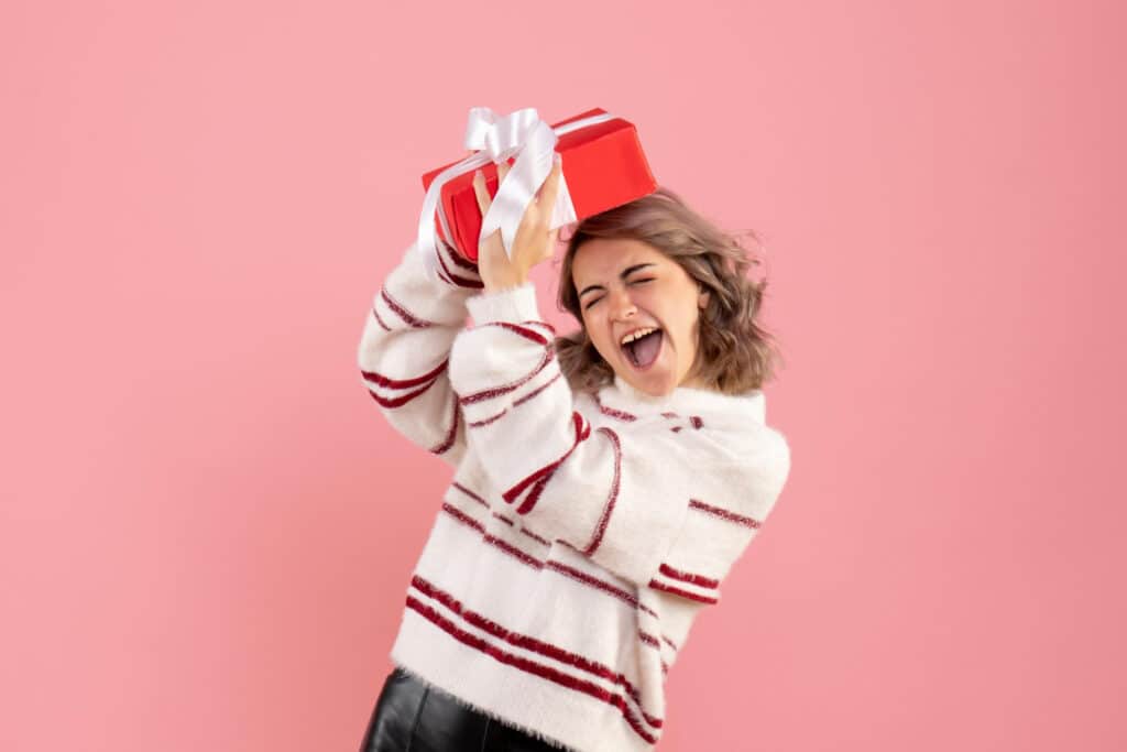 Vrouw met witte trui met rode strepen houdt een rood cadeau met witte strik boven haar hoofd.