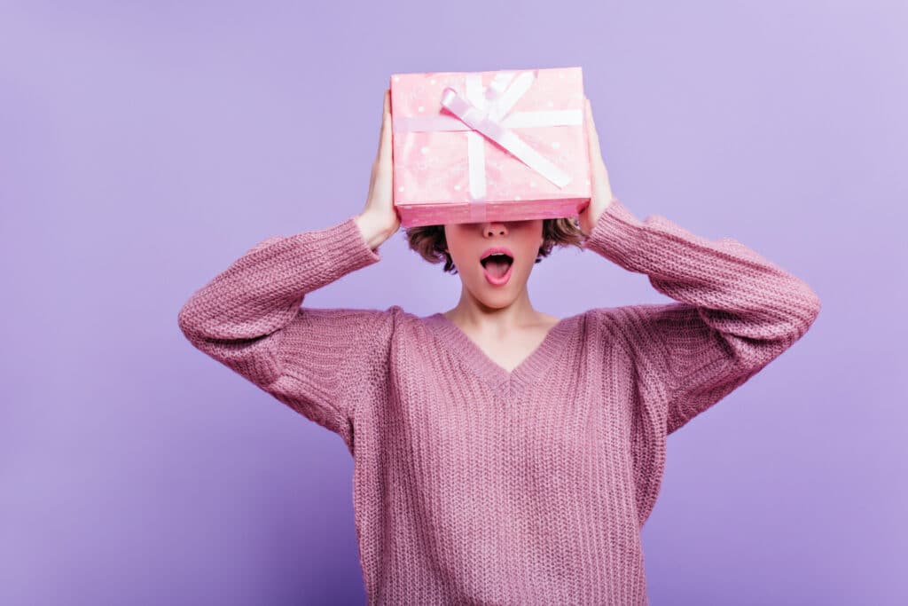 enchanting girl wears woolen sweater isolated purple wall with pink present box indoor photo happy short haired woman having fun with new year gift
