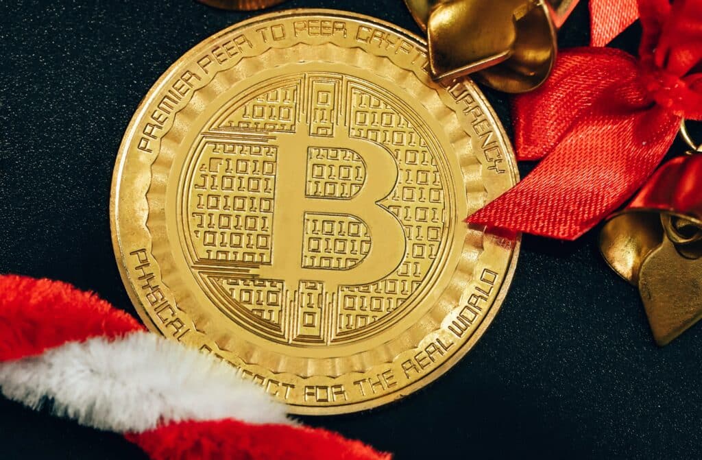 Dit zijn de leukste Bitcoin en crypto geschenken voor de feestdagen 2 Gouden bitcoinmunt met rode en witte kerstversieringen op zwarte achtergrond