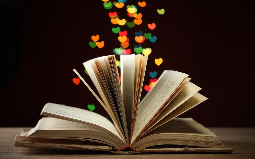 Open boek op houten tafel met kleurrijke hartvormige lichtjes tegen donkere achtergrond.