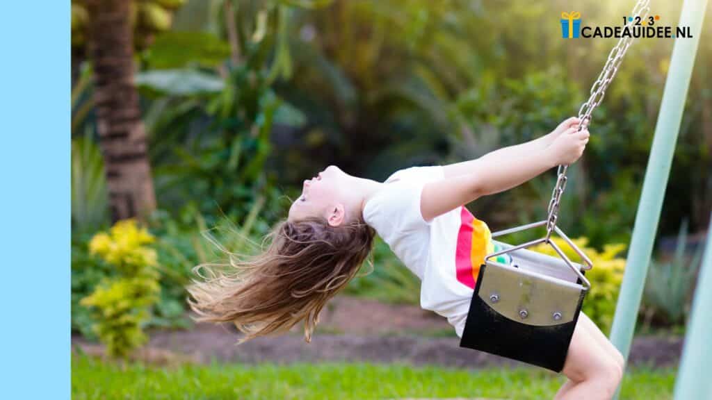 Lachend kind met wapperend haar dat achterover leunt op een schommel in een groene tuin, een perfect cadeau-idee.